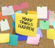 Cork board full of thumbtacked notes including a big one that says MAKE THINGS HAPPEN!