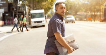 Young pastor carrying a laptop bag while crossing a city street