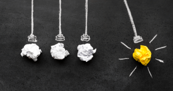 Wadded up paper representing light bulbs in a Newton's cradle. Three are white, and one is yellow, representing an idea. The yellow one is pulled back.